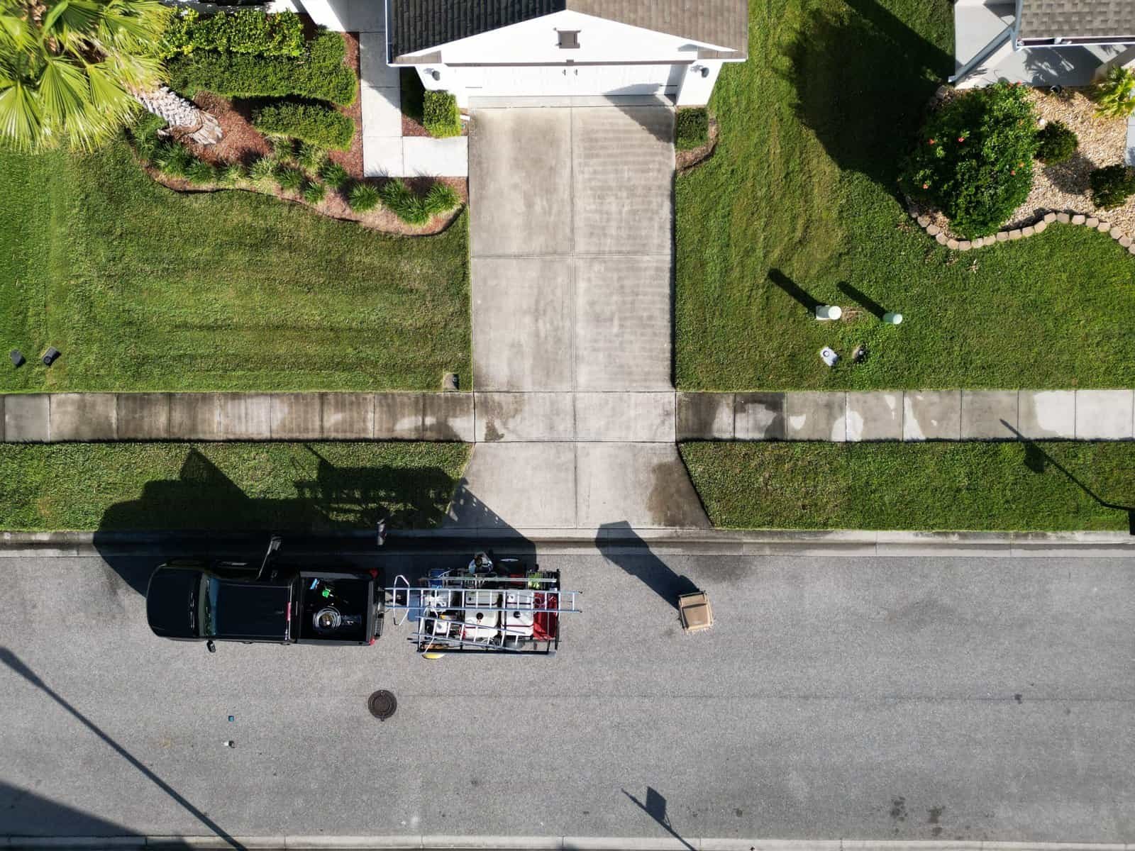 Aerial drone view before driveway cleaning in St. Cloud FL — two-car concrete driveway darkened by algae and black lichen